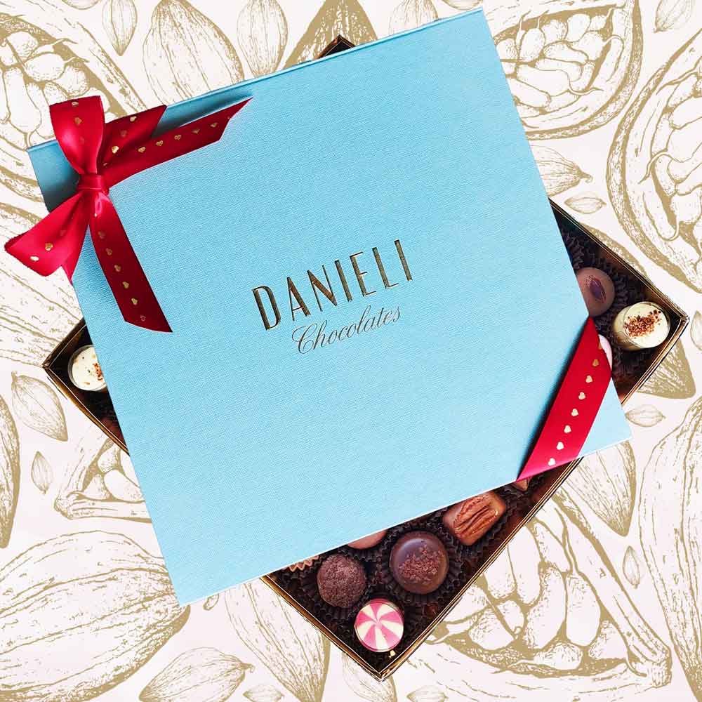 Top view of Danieli extra large box of chocolates for Valentines with a red and gold heart ribbon on a cacao pod background