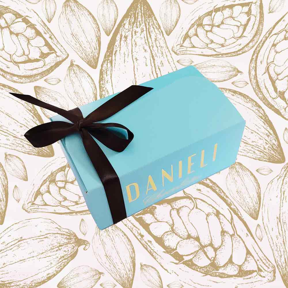 Blue gift box with red ribbon and 'DANIELI' branding on a snowy patterned background