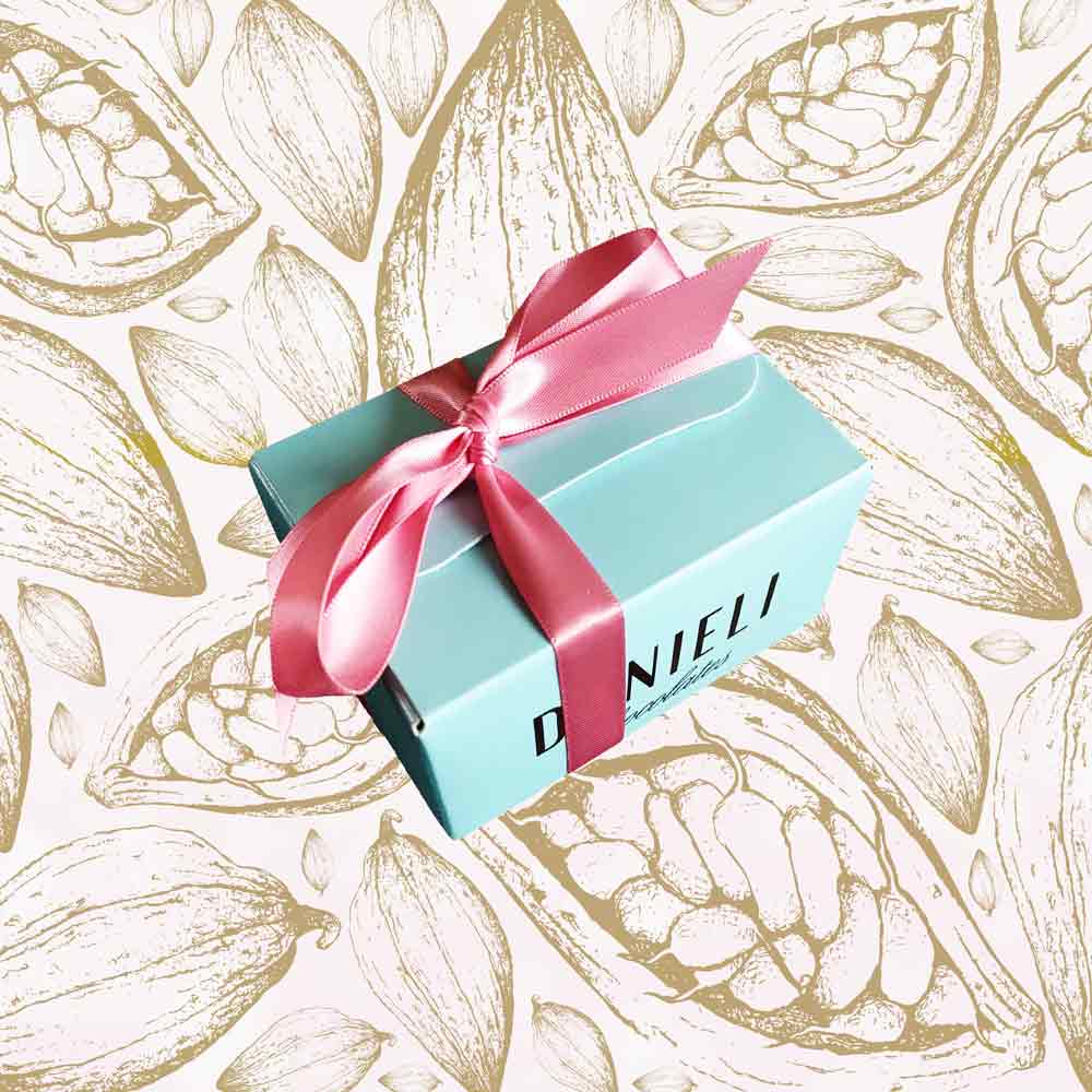 side view of a gift box of Danieli rose and violet chocolate creams on a cacao background