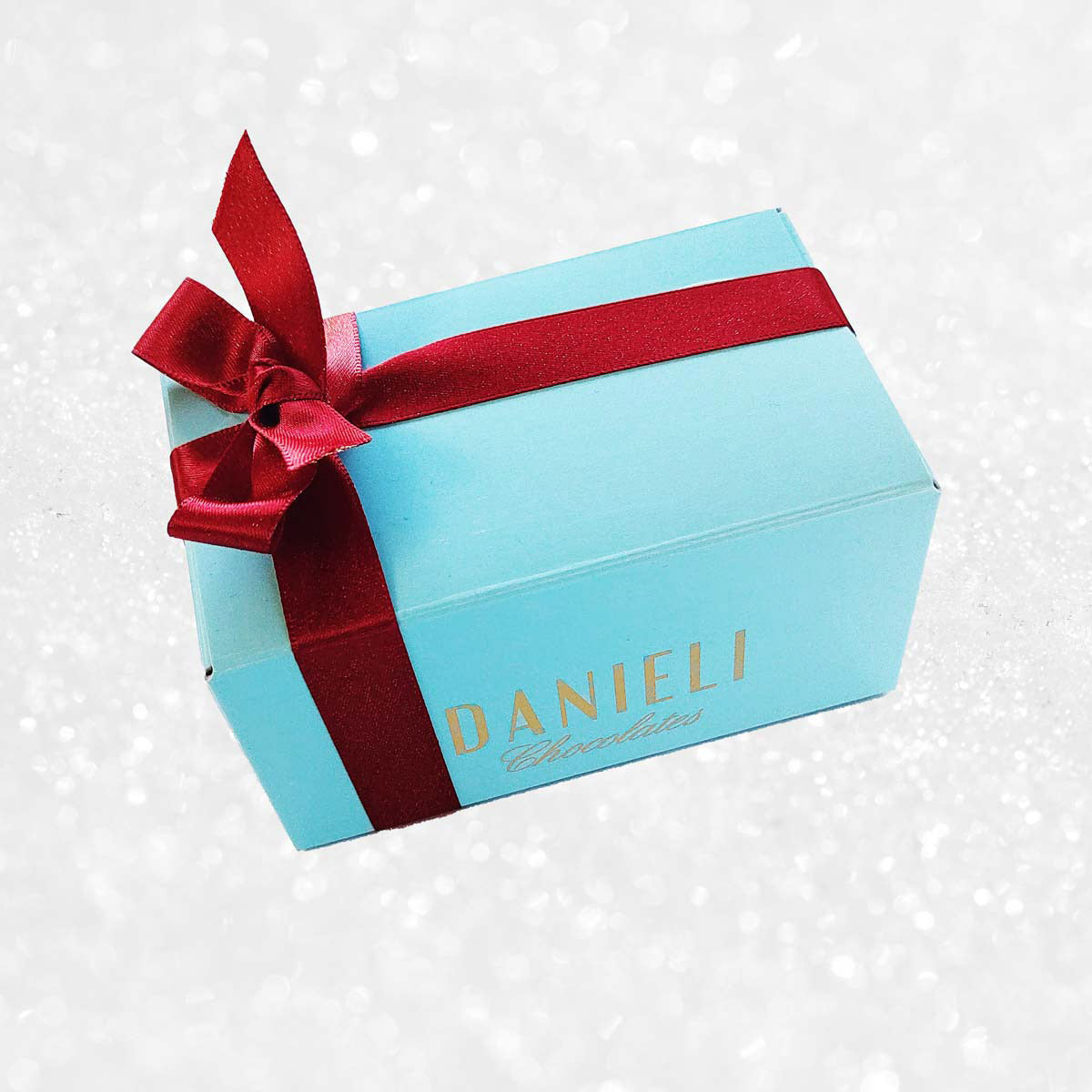 top view of a Danieli chocolate gift box small ballotin with a red ribbon on a snowy background