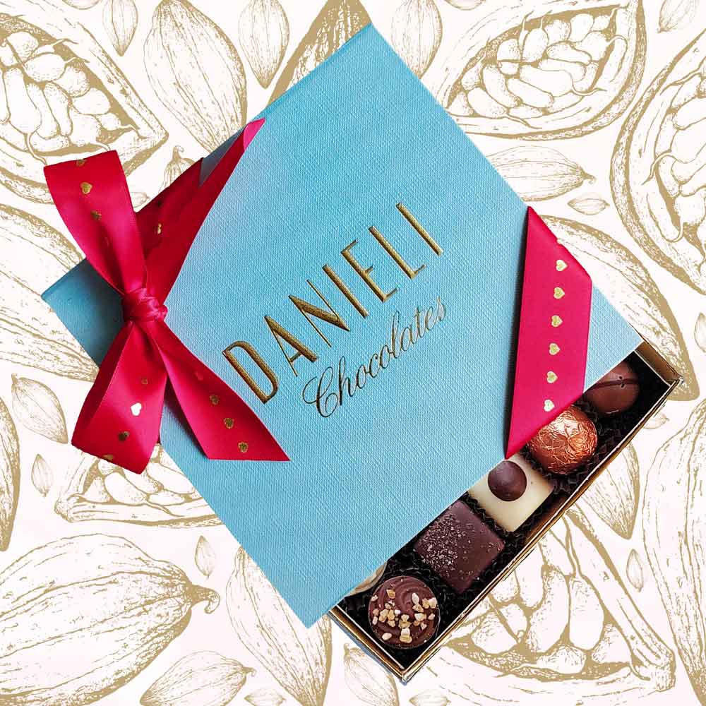 Top view of Danieli small box of chocolates for Valentines with a red and gold heart ribbon on a cacao pod background