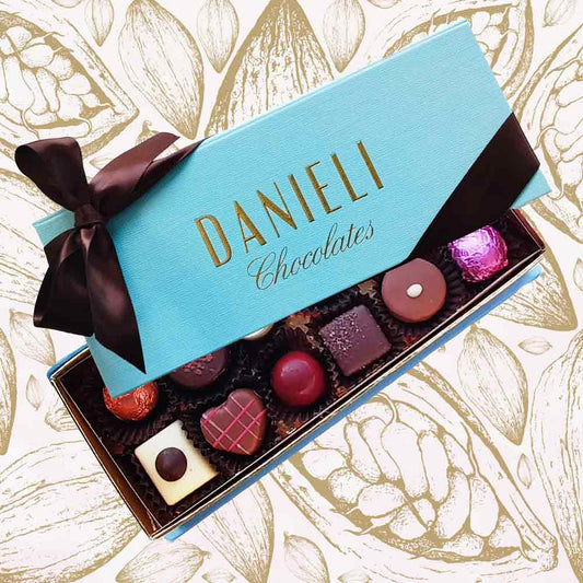 Box of Danieli Chocolates with a turquoise lid and brown ribbon on a decorative background.