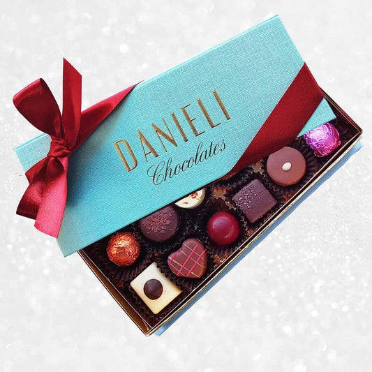 Box of Danieli Chocolates with a turquoise lid and red ribbon on a decorative background.