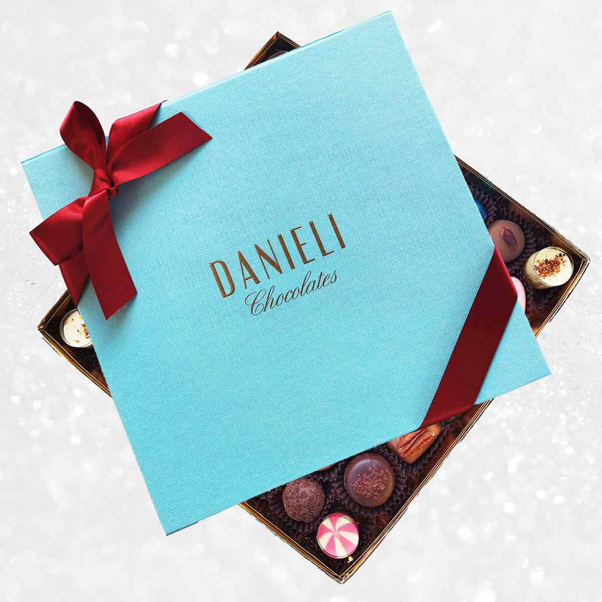 Blue box of Danieli Chocolates with a red ribbon on a decorative background