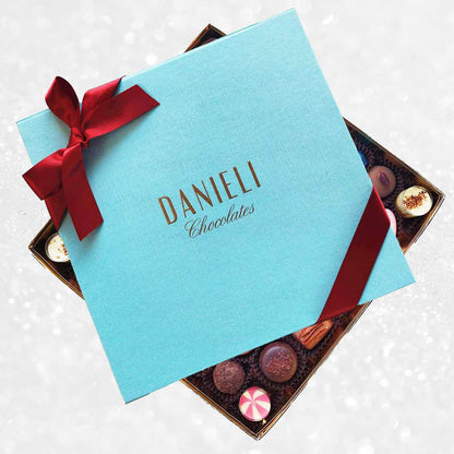 Blue box of Danieli Chocolates with a red ribbon on a decorative background