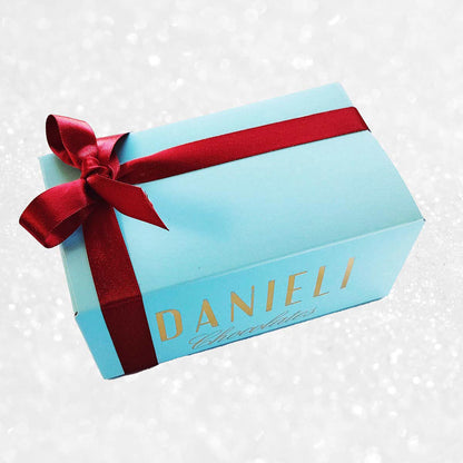 Blue gift box with red ribbon and 'DANIELI' branding on a snowy patterned background