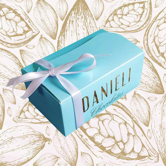top view of a Danieli chocolate gift box large ballotin with a white satin ribbon on a cacao pod background