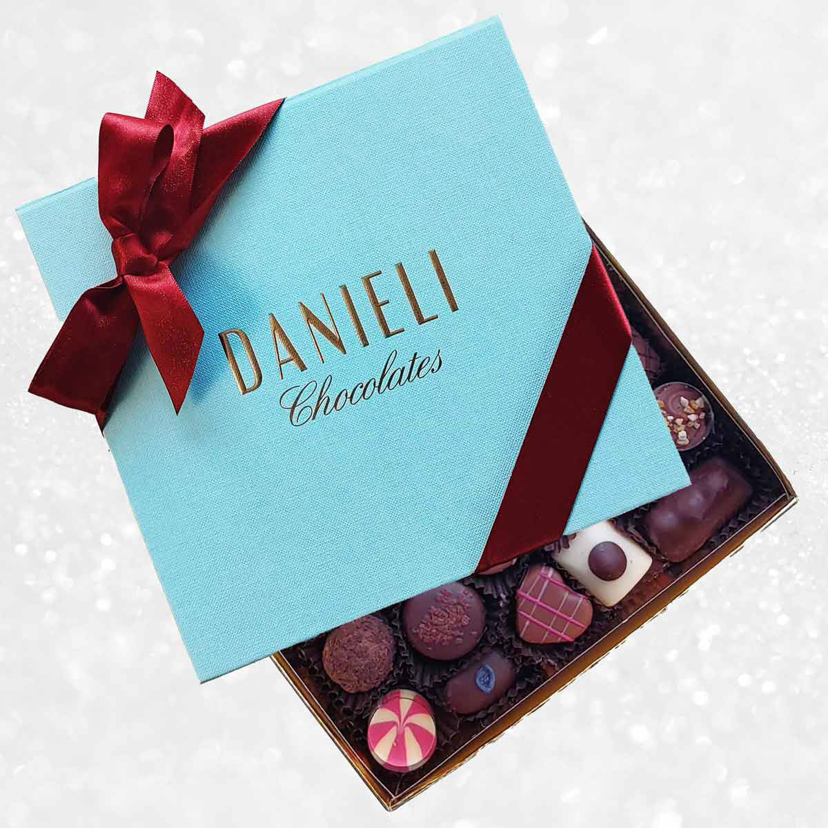 Blue box of Danieli Chocolates with a red ribbon on a decorative background