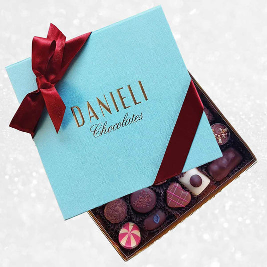 Blue box of Danieli Chocolates with a red ribbon on a decorative background