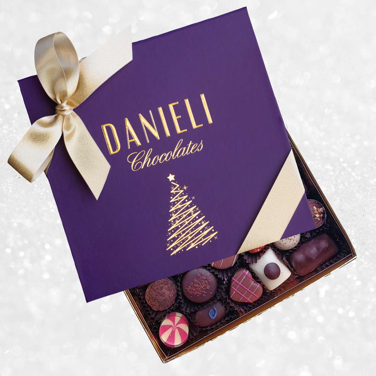 Box of Danieli Chocolates with a purple lid featuring a gold bow and Christmas tree design.