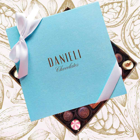 top view of a Danieli chocolate gift box extra large with a white satin ribbon on a cacao pod background