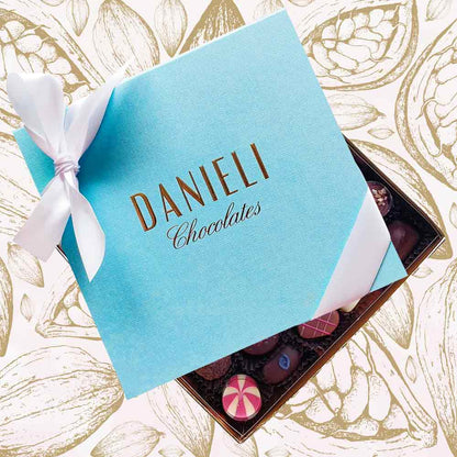 top view of a Danieli chocolate gift box large with a white satin ribbon on a cacao pod background