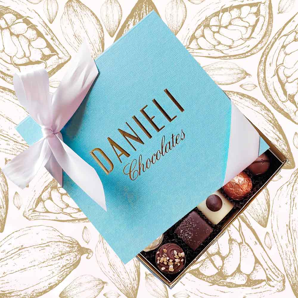 top view of a Danieli chocolate gift box small with a white satin ribbon on a cacao pod background