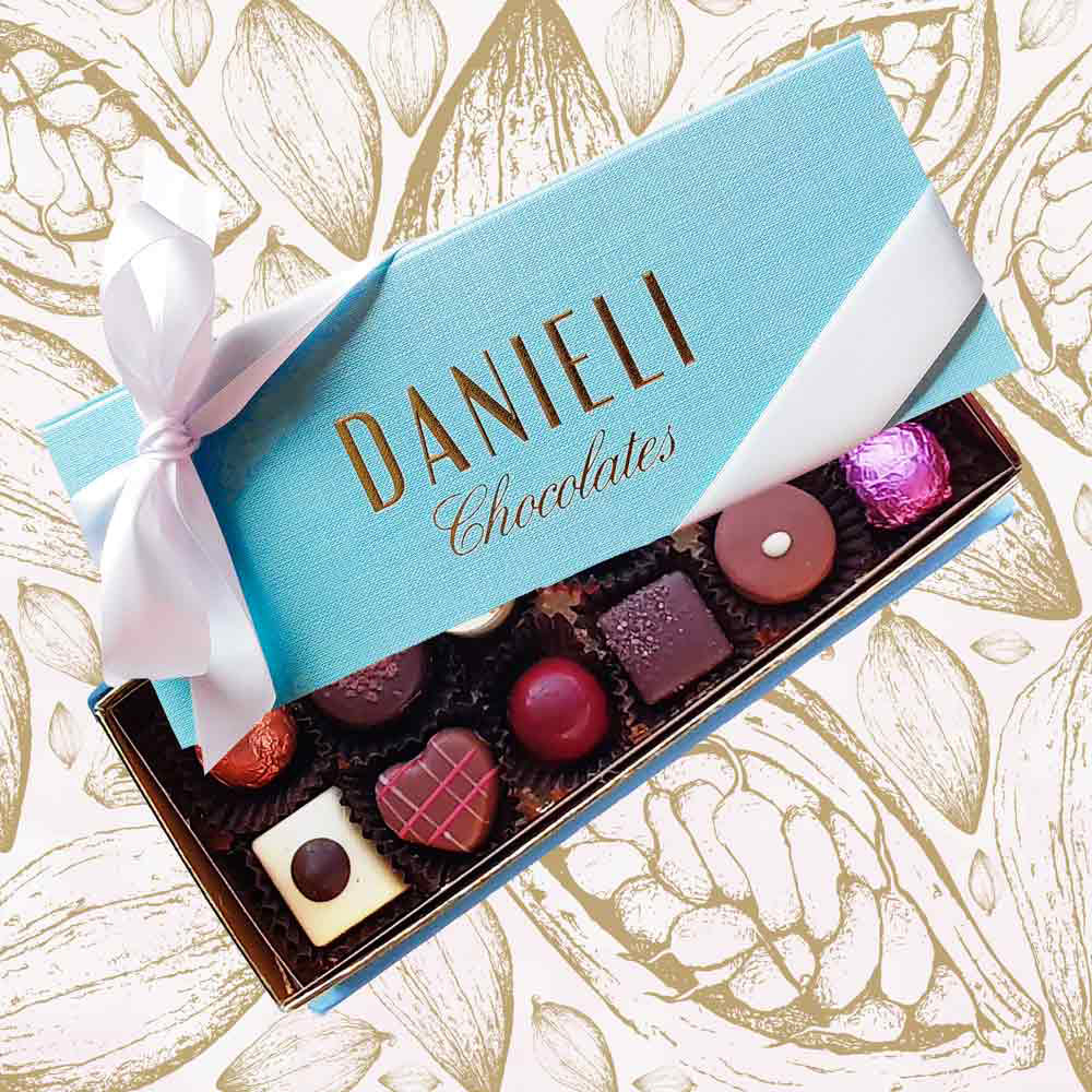 top view of a Danieli chocolate gift box with 12 chocolates with a white satin ribbon on a cacao background