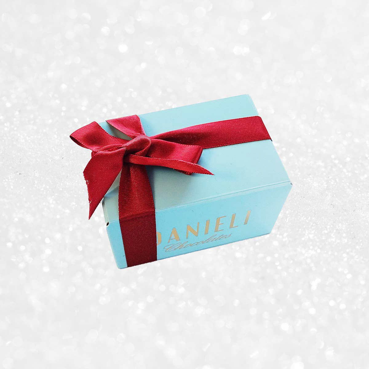 Blue chocolate gift box with red ribbon on a snowy background  