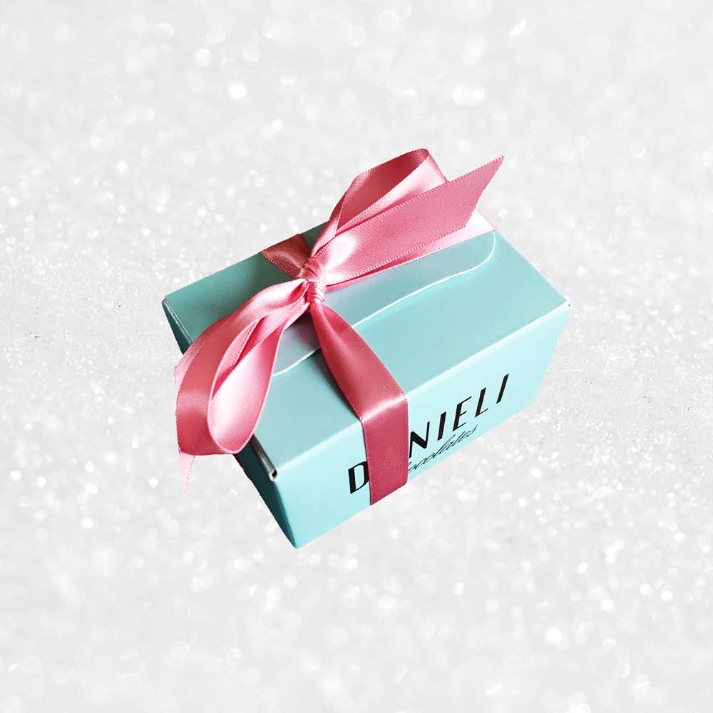 side view of a gift box of Danieli rose and violet chocolate creams on a snowy background