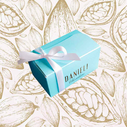 top view of a Danieli chocolate gift box small ballotin with a white satin ribbon on a cacao pod background