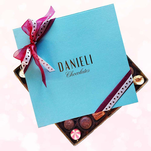 top view of a Danieli extra large chocolate gift box with a heart ribbon on a pink background