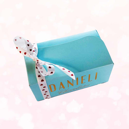 Side view of Danieli chocolates for Valentines large ballotin with a pretty heart ribbon on a pink heart background