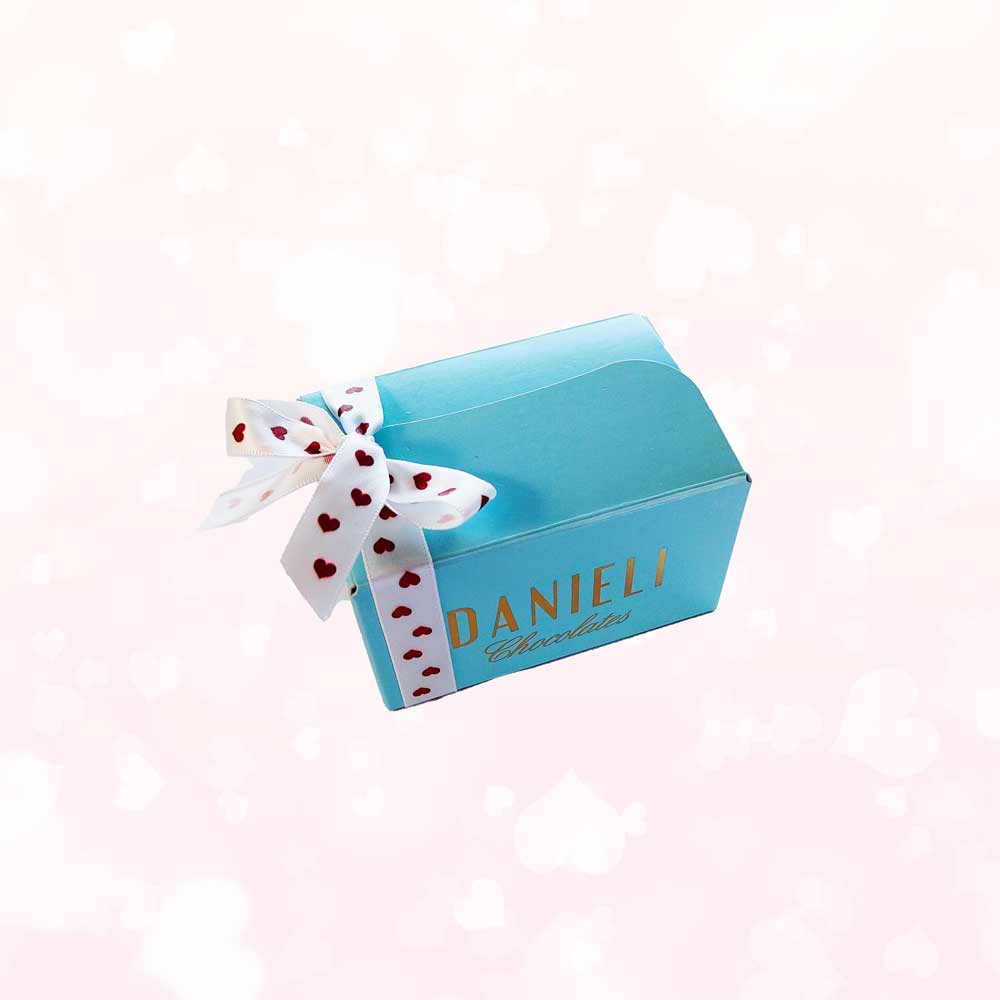 Side view of Danieli chocolates for Valentines mini ballotin with a pretty heart ribbon on a pink heart background