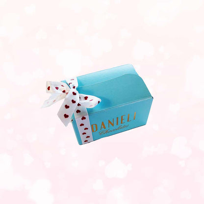 Side view of Danieli chocolates for Valentines mini ballotin with a pretty heart ribbon on a pink heart background