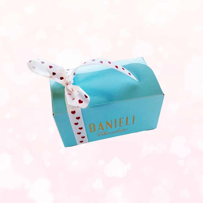 Side view of Danieli chocolates for Valentines small ballotin with a pretty heart ribbon on a pink heart background